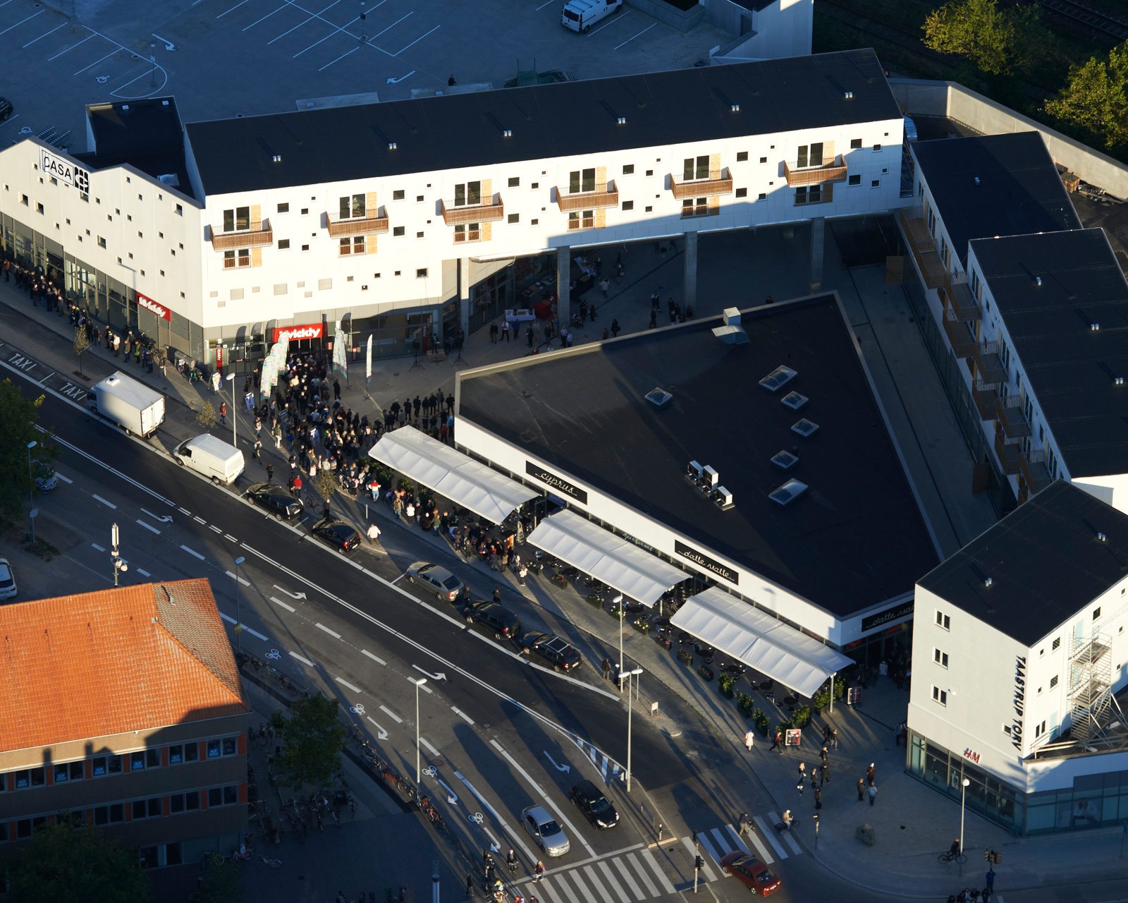Dronebillede. En stor flok mennesker står i kø til åbningen af Taastrup Torvs butikscenter. Man kan se lejlighederne, som er placeret i et V omring centeret.