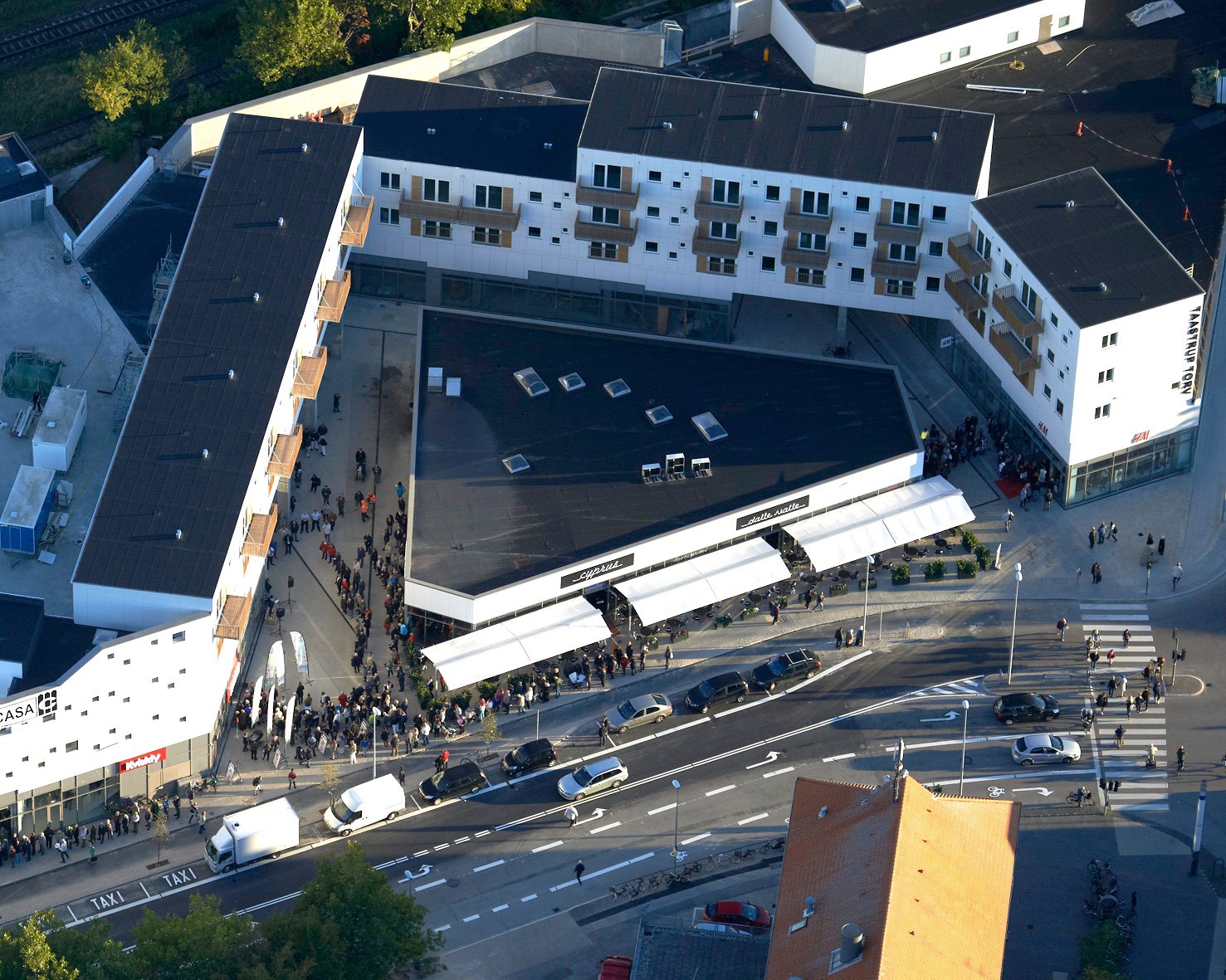 Dronebillede. En stor flok mennesker står i kø til åbningen af Taastrup Torvs butikscenter. Man kan se lejlighederne, som er placeret i et V omring centeret.