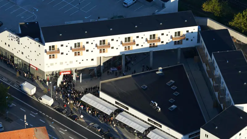Dronebillede. En stor flok mennesker står i kø til åbningen af Taastrup Torvs butikscenter. Man kan se lejlighederne, som er placeret i et V omring centeret.