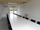 Et langt hvidt bord i et mødelokale, billedet er taget fra den ene ende og ned mod vinduerne i bagvæggen. Der er sorte stole og hvide vægge.